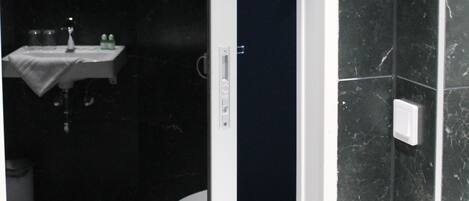 Un baño con pared de mármol oscuro, un lavamanos blanco y un inodoro.