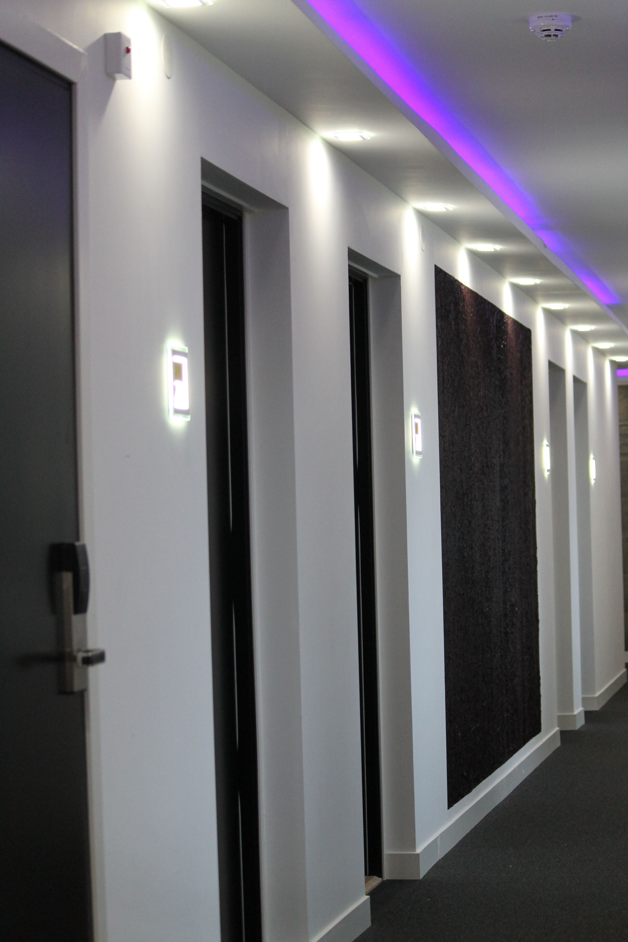A hallway with white walls, black doors, and a dark textured wall.