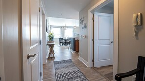 Un pasillo con un tapete estampado, una zona de comedor con mesa y sillas, y una cocina a la vista en el fondo.