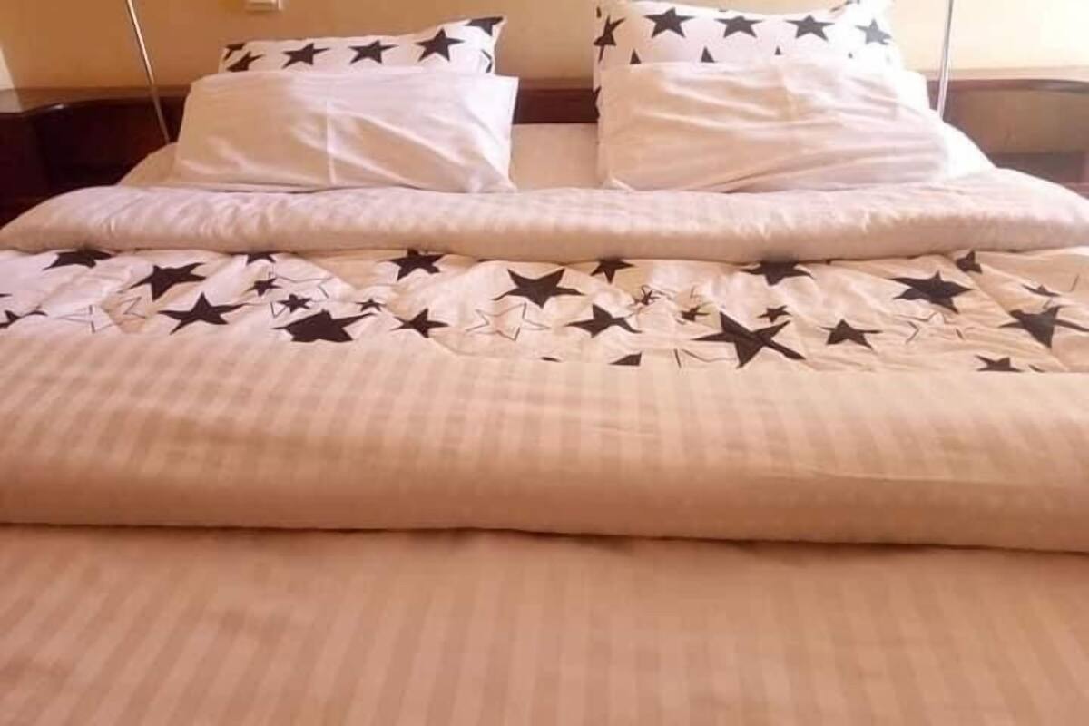A bed with a beige bedspread featuring a star pattern, white pillows, and a wooden headboard.