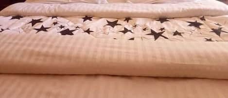 Una cama con colcha color beige con diseño de estrellas, almohadas blancas y cabecera de madera.