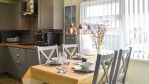 Un comedor con una mesa dispuesta para dos, una cocina al fondo y una ventana con cortinas.
