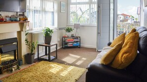 Una sala de estar con chimenea, un sofá con cojines, una mesa de centro, una estantería y una ventana con vistas al exterior.
