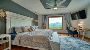 A bedroom with a bed, a desk, a chair, a TV, and a window with a view of greenery. - Meribel-Hot tub-Fire pit-Amazing Views (Young Harris)