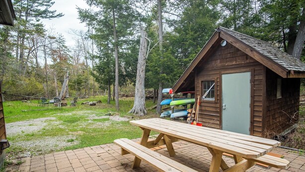 Eine Holzhütte mit Picknicktisch davor, umgeben von Bäumen.