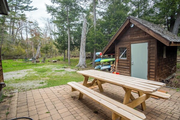 A wooden cabin with a picnic table in front, surrounded by trees.