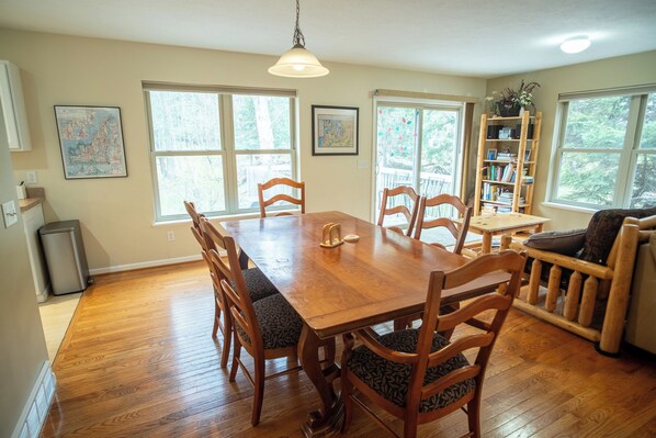 A dining area with a wooden table and chairs, a hanging light fixture, and a bookshelf.