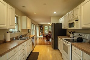 A kitchen with white cabinets, a black refrigerator, a microwave, a stove, and a dining area with chairs and a table.