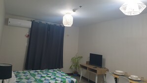 A hotel room with a bed, a desk with a TV, a potted plant, and a dining table set for two.