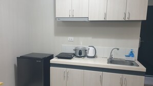 A compact kitchen with a black refrigerator, a kettle, a coffee maker, and a sink.