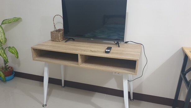 A wooden TV stand with a flat-screen TV, a remote, and a small basket.