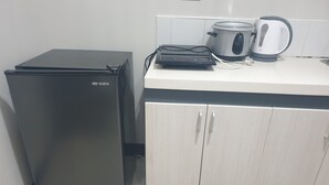 A compact kitchen with a black refrigerator, a white countertop, a kettle, and a slow cooker.