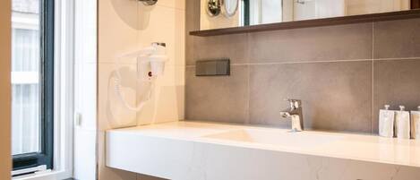 A modern bathroom with a white sink, a mirror, a towel rack, and a window.
