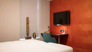 A hotel room with a bed, a desk with a TV, a lamp, and a chair.