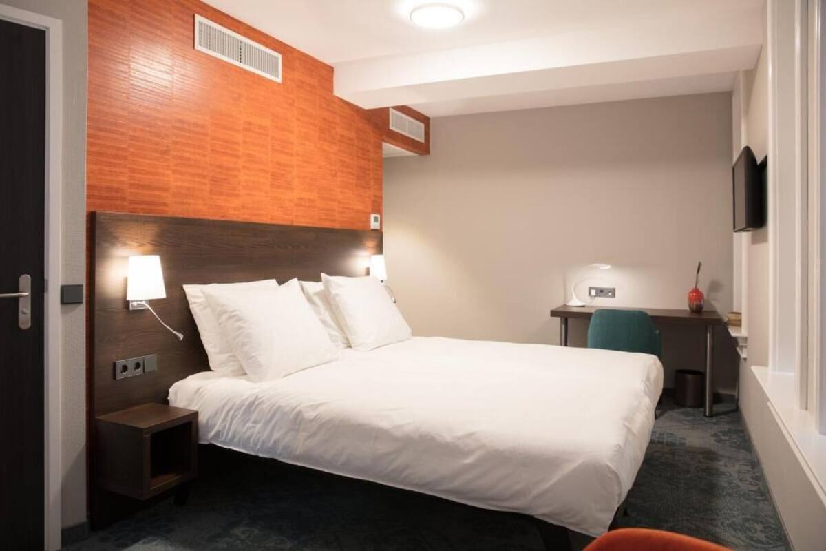 A hotel room with a large bed, a desk, and a chair.