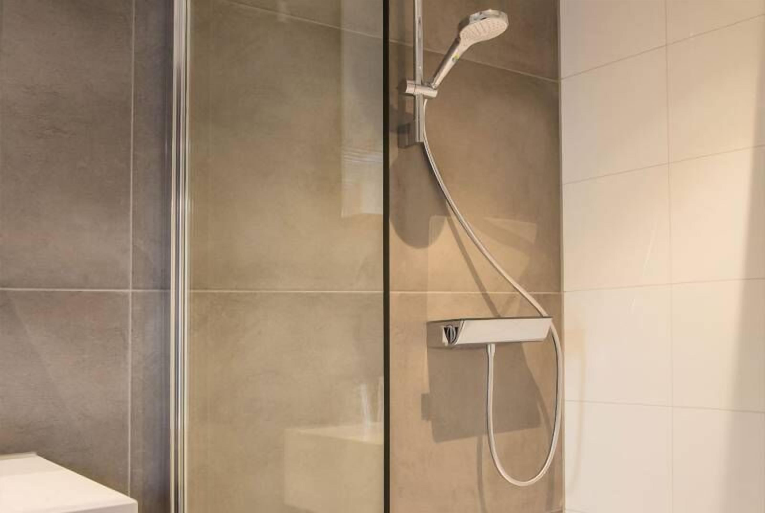 A modern bathroom with a glass shower enclosure, a handheld showerhead, and a wall-mounted control panel.