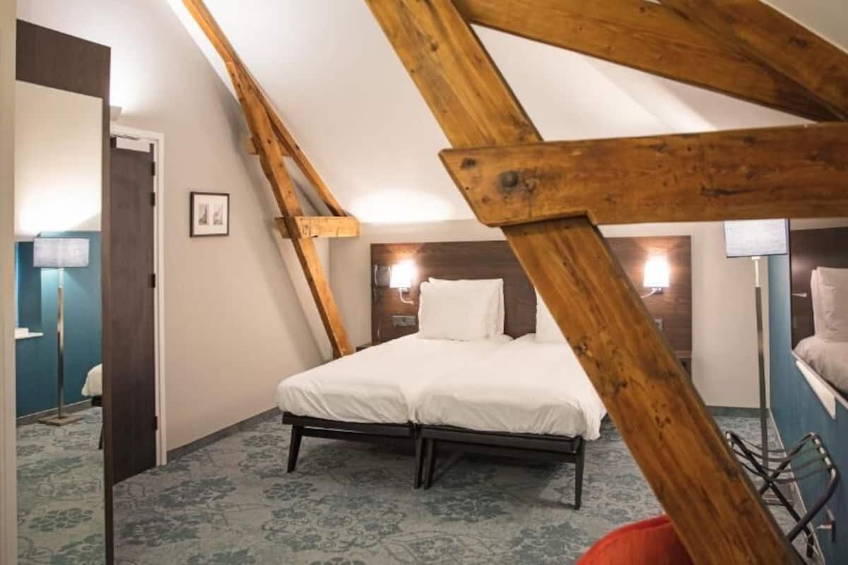 A bedroom with a sloped ceiling, a bed with white bedding, a wooden headboard, and a blue carpet.