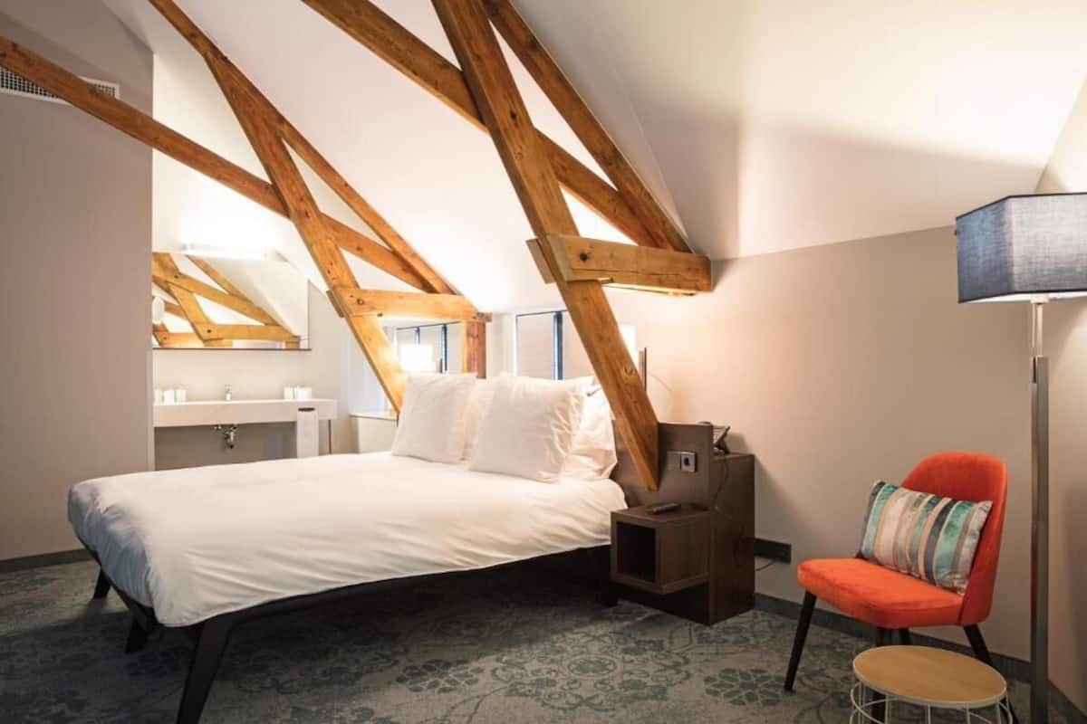 A bedroom with a bed, a nightstand, a chair, and a lamp.