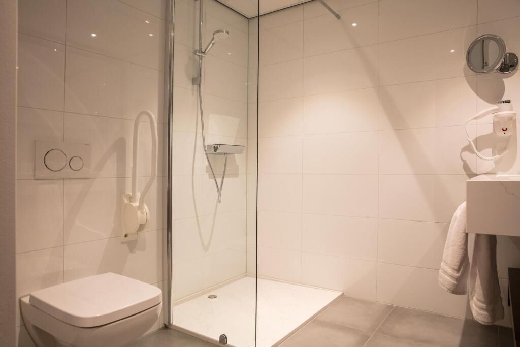 Un baño moderno con ducha de vidrio, inodoro blanco y lavamanos con una toalla colgada en la pared.