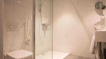 Un baño moderno con ducha de vidrio, inodoro blanco y lavamanos con una toalla colgada en la pared.
