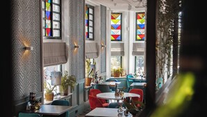 A restaurant interior with multiple tables and chairs, large windows with colorful stained glass, and a patterned wall. - Hotel de Koppelpaarden (Lichtenvoorde)
