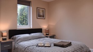 Quarto com uma cama, duas luminárias de cabeceira, uma janela e um quadro na parede.