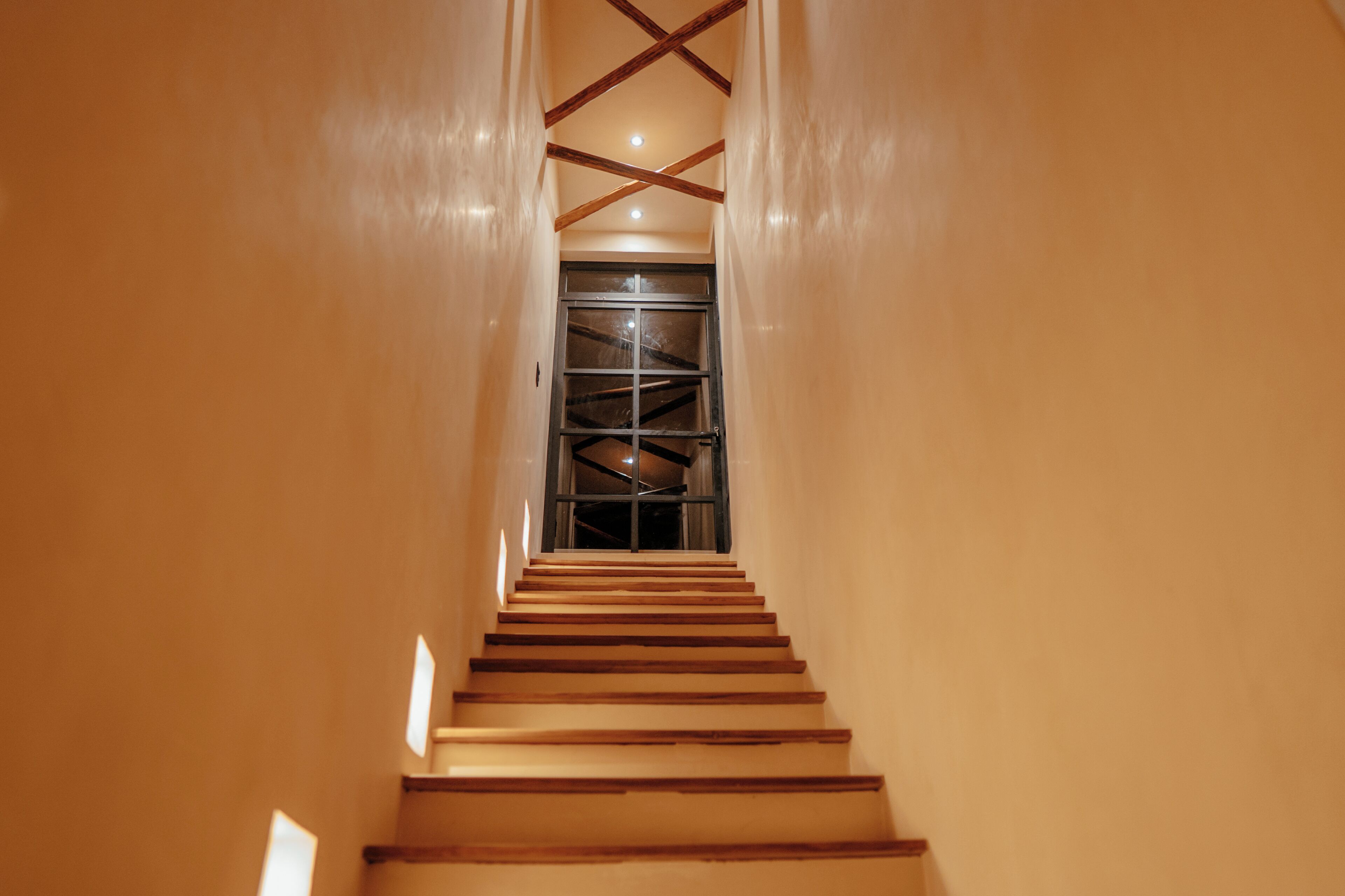 A staircase leading to a room with a large window and a ceiling with wooden beams.