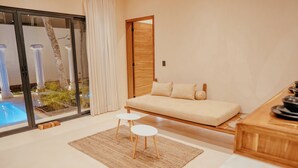 Ein modernes Wohnzimmer mit einer Couch, zwei kleinen Hocker, einem Holztisch und einer Glastür zum Poolbereich.