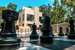A chessboard with chess pieces in front of a building with large windows and a stone facade.