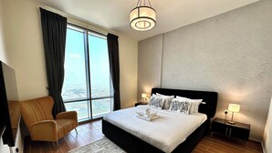 Una camera d'albergo moderna con un letto grande, vista sulla città, un divano e un comodino con una lampada.