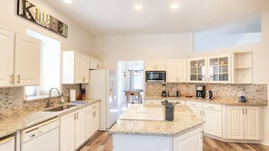A modern kitchen with white cabinetry, granite countertops, and a central island. - Five Star 3bd Waterfront Canal Home w/ Private Pool/Spa & Boat Dock. (Palm Coast)