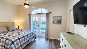 A bedroom with a bed, a ceiling fan, a TV, a window with curtains, and a painting on the wall. - Five Star 3bd Waterfront Canal Home w/ Private Pool/Spa & Boat Dock. (Palm Coast)