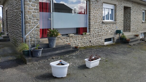 A stone house with a balcony, potted plants, and a visible mailbox.