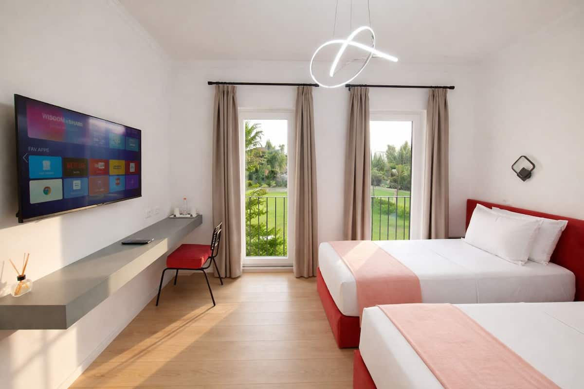 Une chambre d’hôtel équipée d’une télévision, d’un bureau avec une chaise, de deux lits et d’un balcon avec des rideaux.