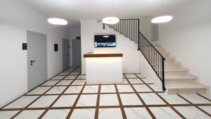 Un hall d’hôtel moderne avec un comptoir d’accueil, un téléviseur à écran plat, un escalier et un sol carrelé.