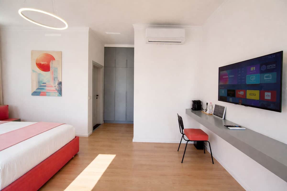 Une chambre d’hôtel moderne équipée d’un lit, d’un bureau, d’une chaise et d’un grand écran numérique affichant diverses applications.