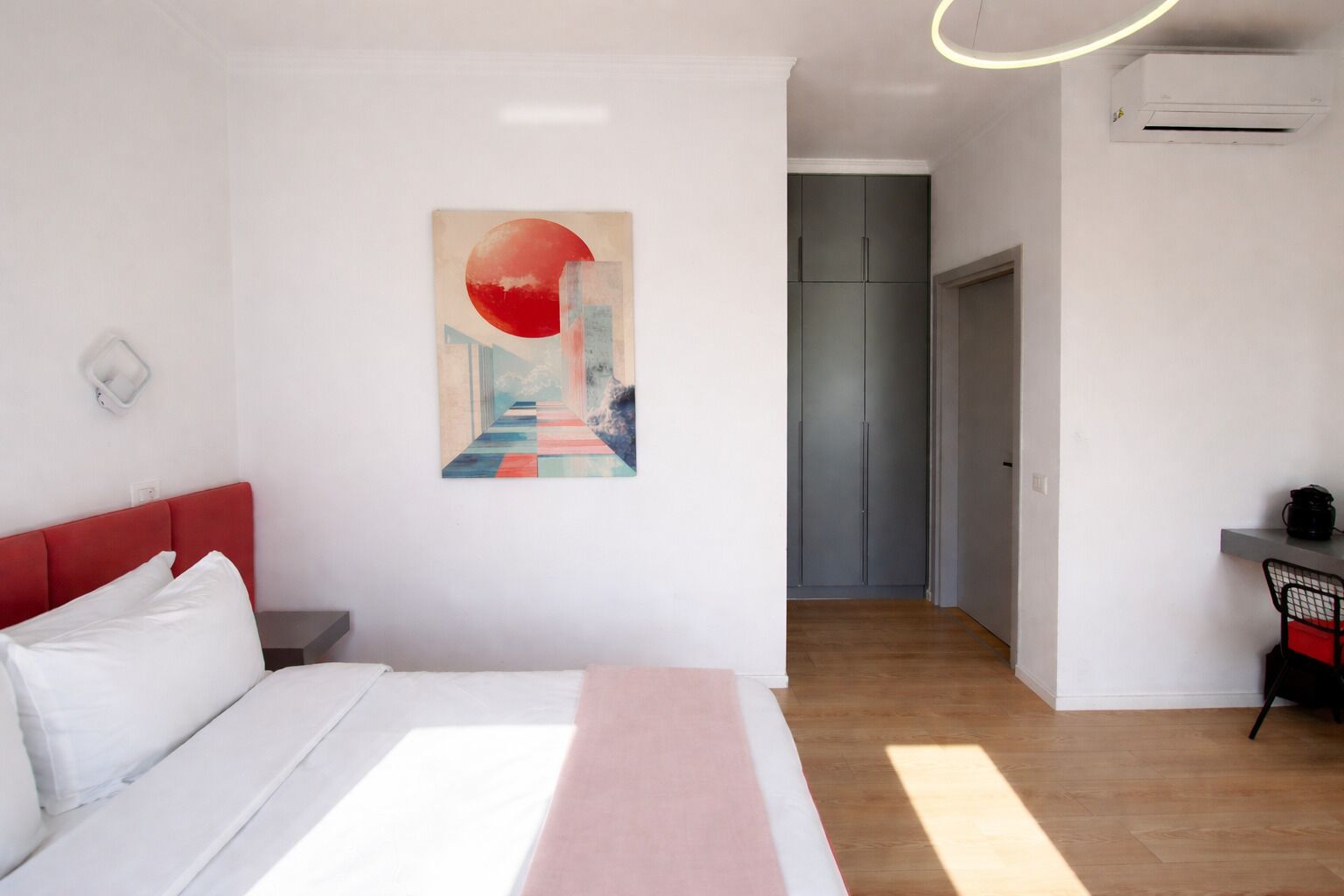 Una habitación de hotel moderna con una cama, un cuadro, un escritorio y un armario.