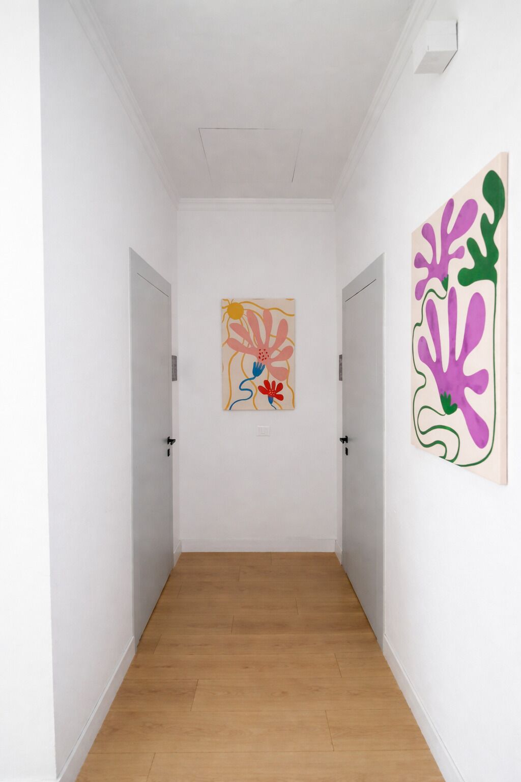 A hallway with wooden flooring, white walls, and two doors.