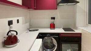 Une cuisine avec un meuble rouge, une bouilloire, un grille-pain, un lave-vaisselle et un four.