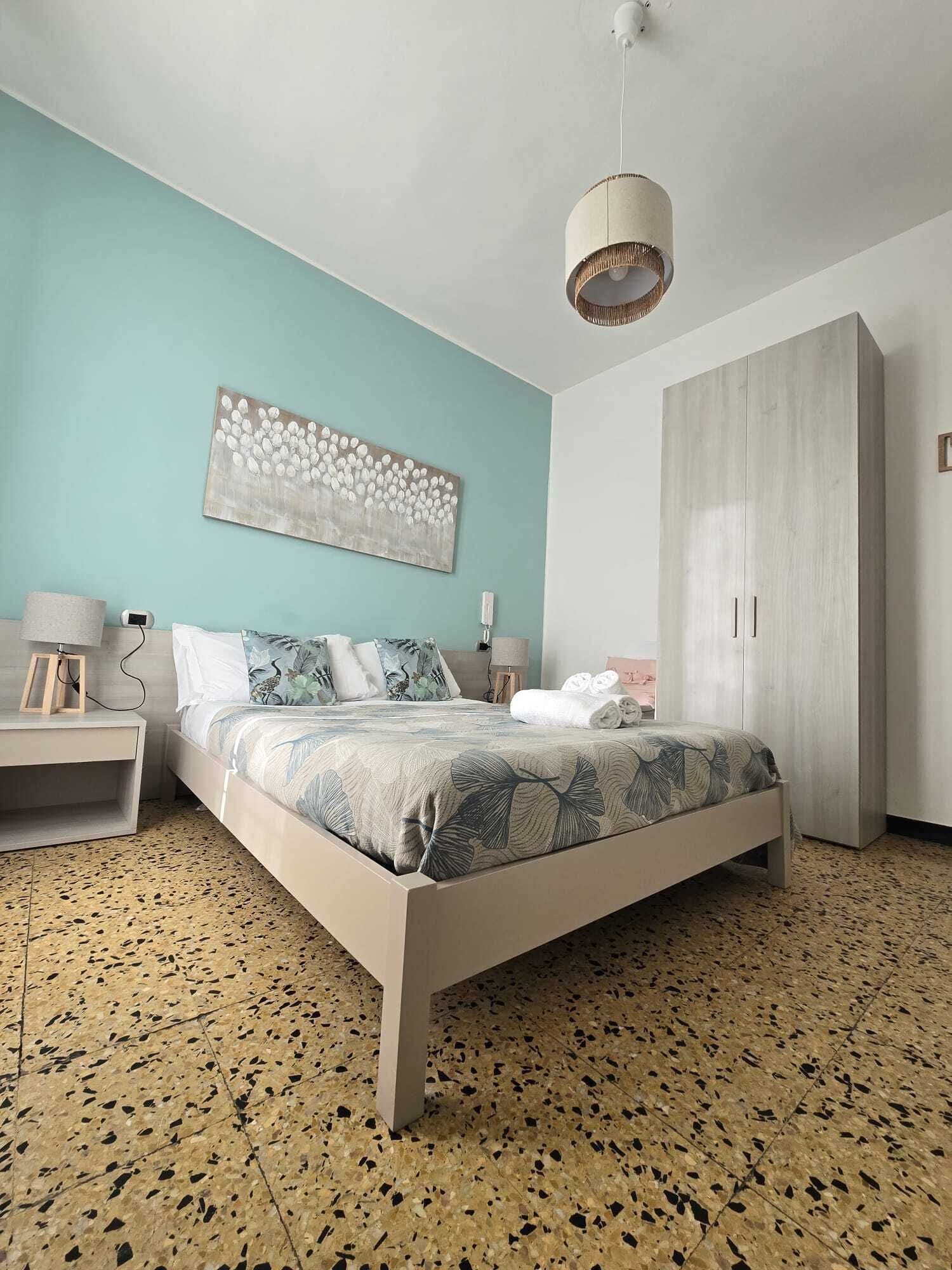 A bedroom with a bed, a nightstand, a wardrobe, a hanging light, and a wall art piece.