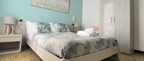 A bedroom with a bed, a nightstand, a wardrobe, a hanging light, and a wall art piece.