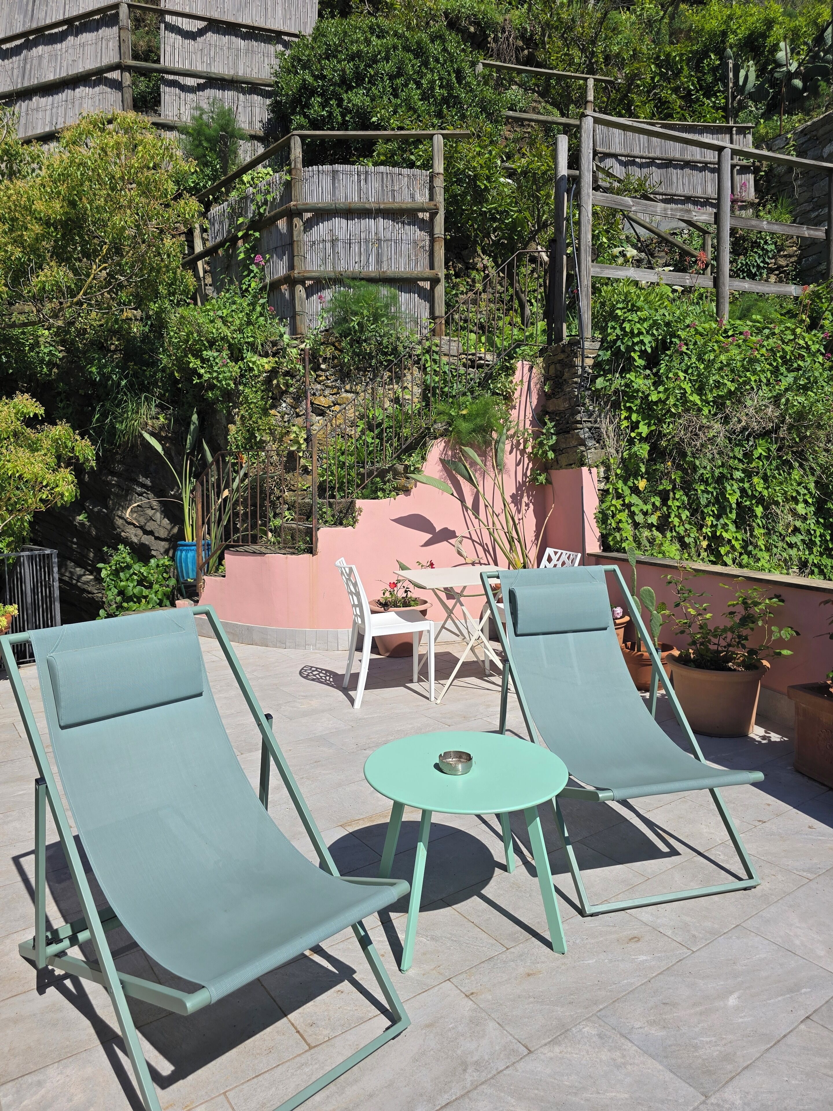 A rooftop patio with two green lounge chairs, a small round table, and a white chair.