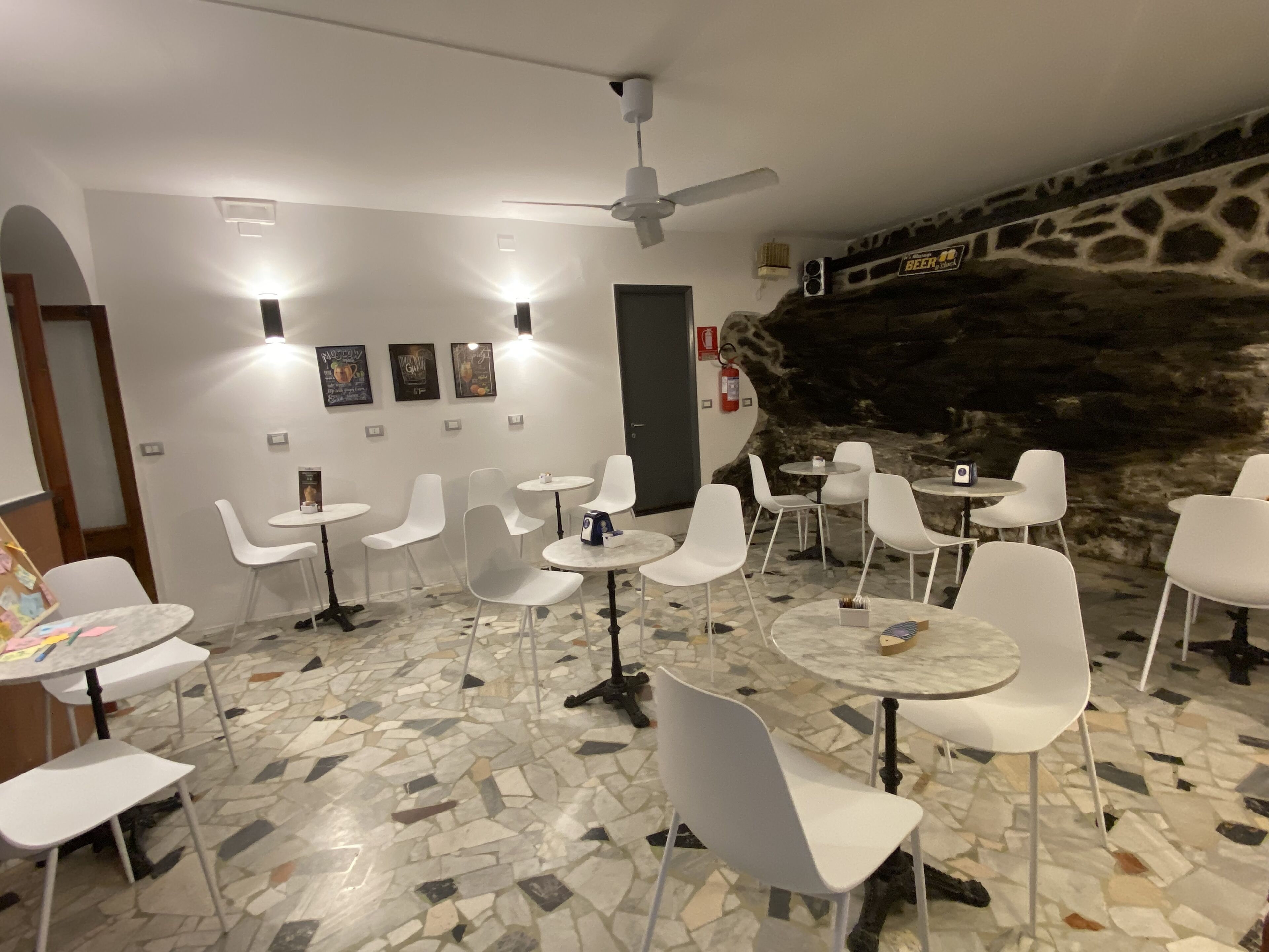 Un intérieur moderne avec des chaises et des tables blanches, un ventilateur de plafond et un mur en pierre.