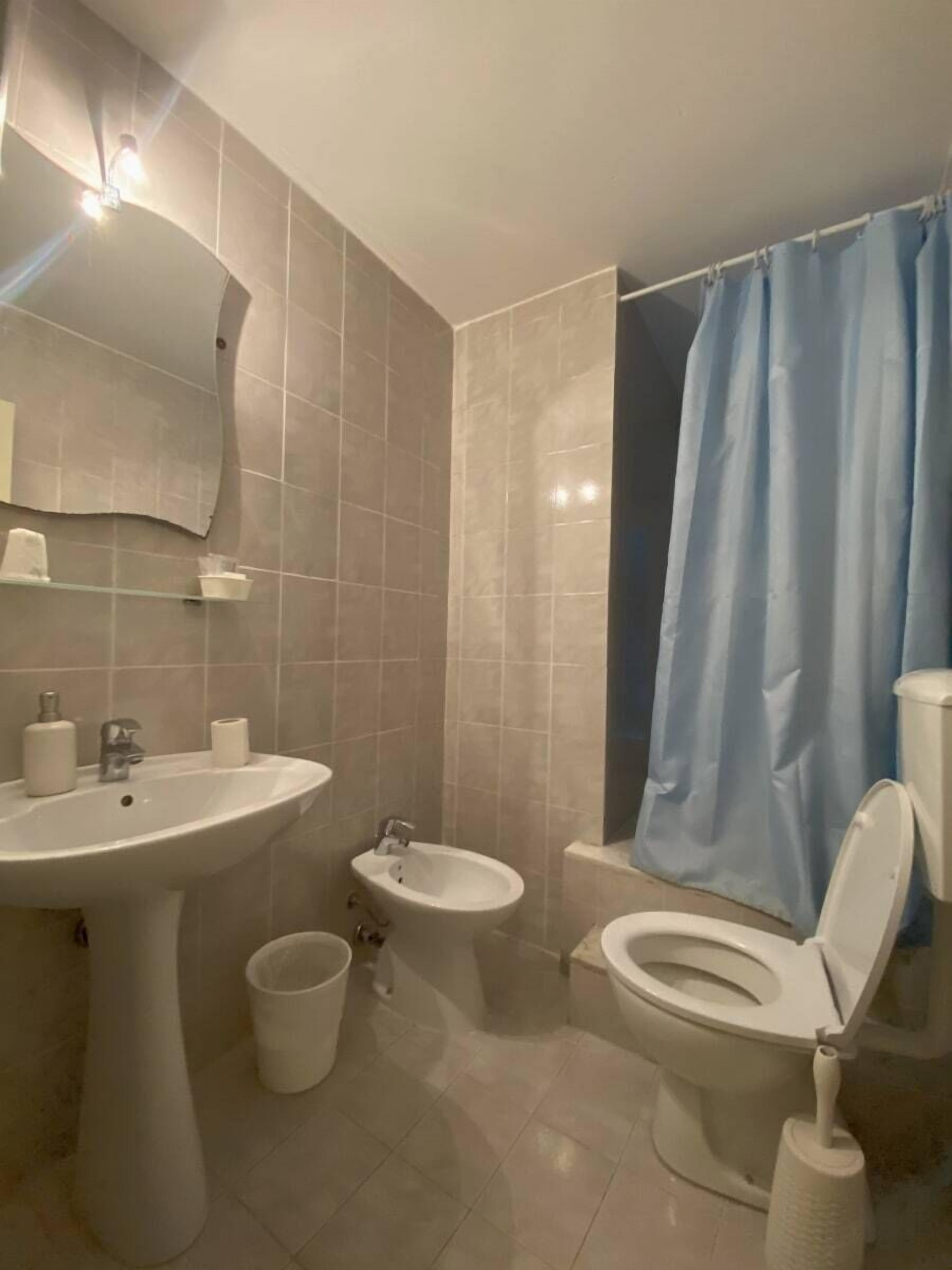 Un baño con lavamanos, bidé, inodoro y una cortina de ducha azul.