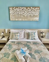 Una cama bien tendida con ropa de cama de motivos florales, dos almohadas con diseños de peces y un cuadro de tulipanes colgado en la pared.
