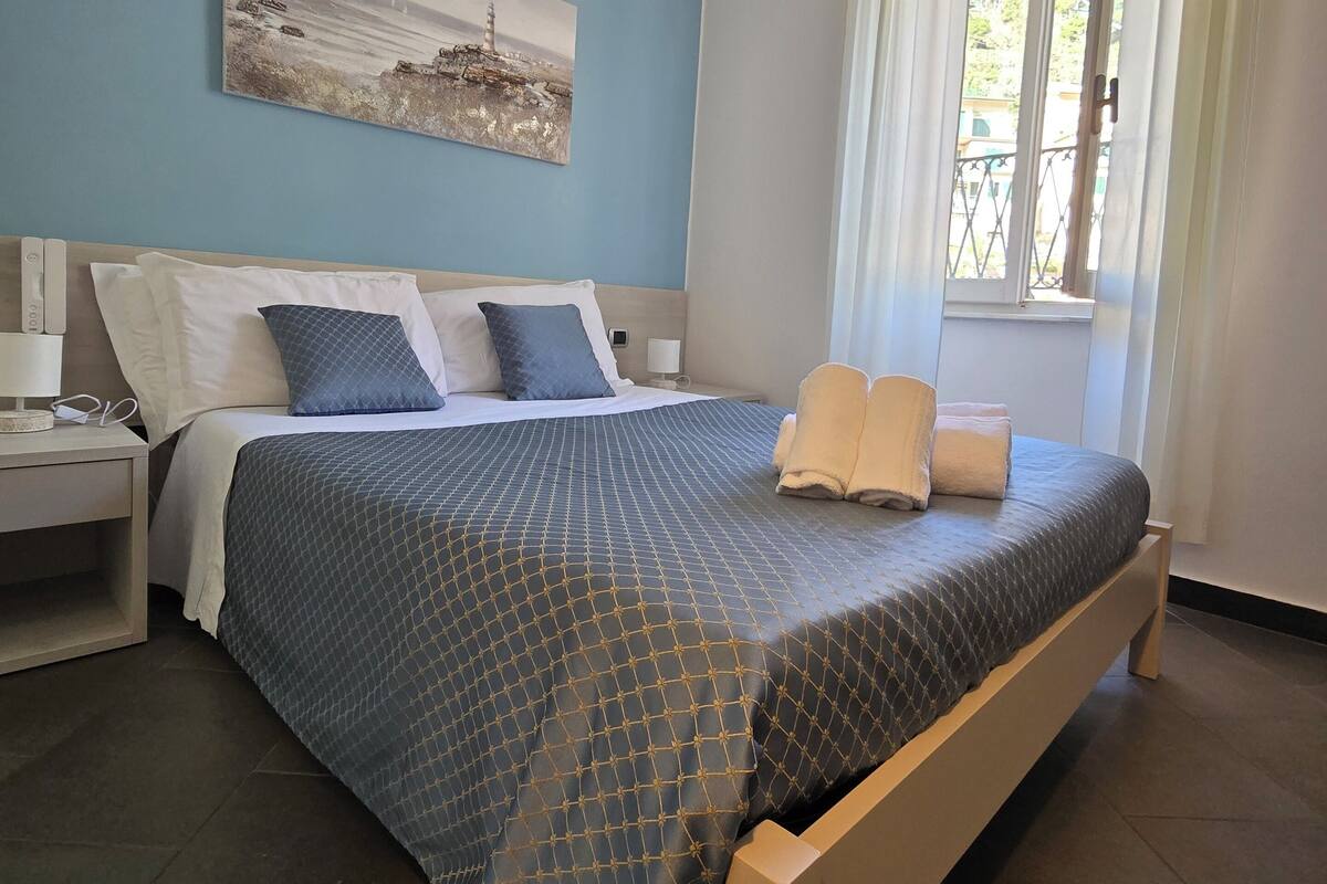 A bedroom with a bed, a nightstand, a window with curtains, and a wall-mounted picture.
