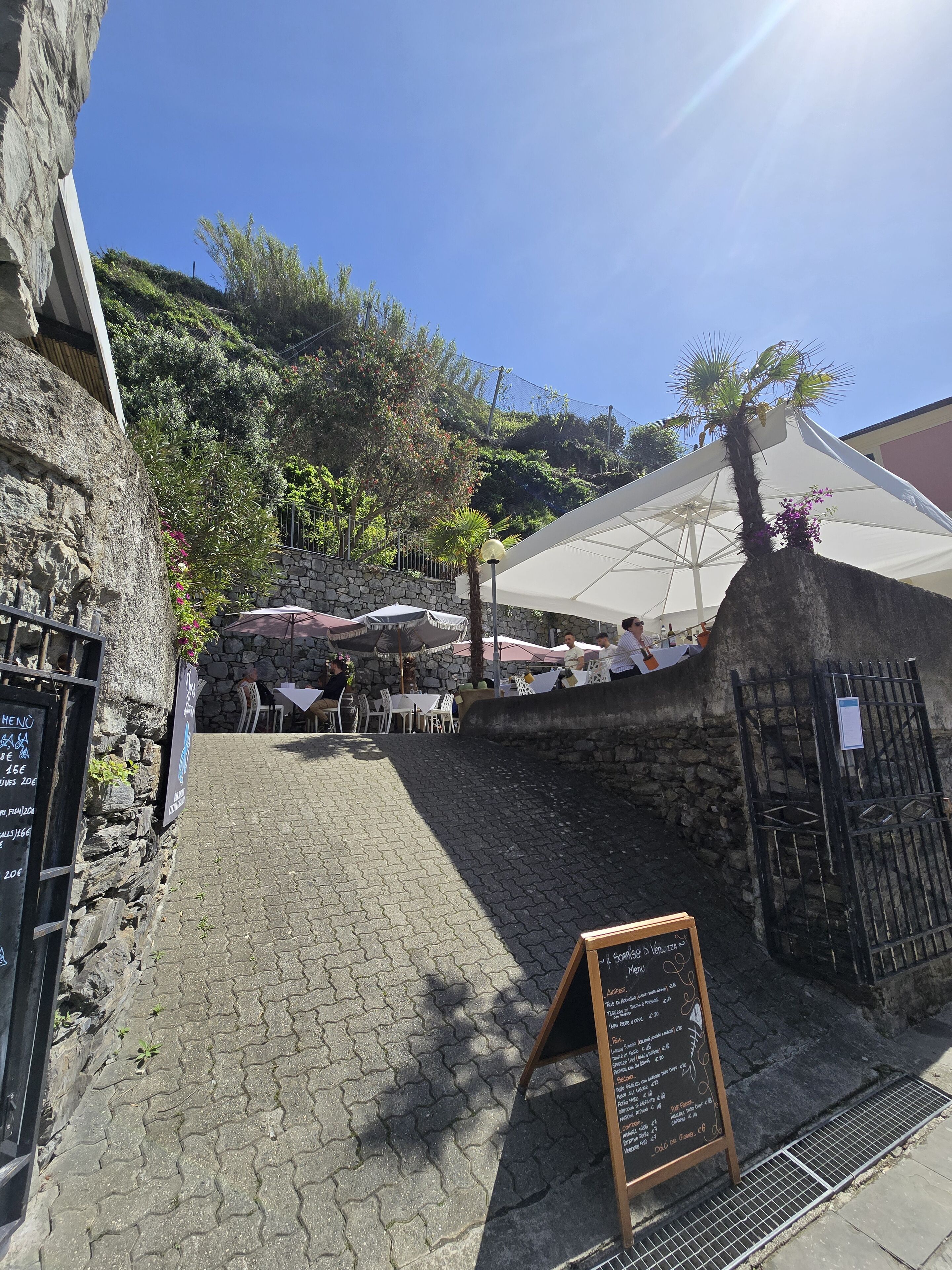 A stone building with outdoor seating and umbrellas, a chalkboard menu, and a stone wall.