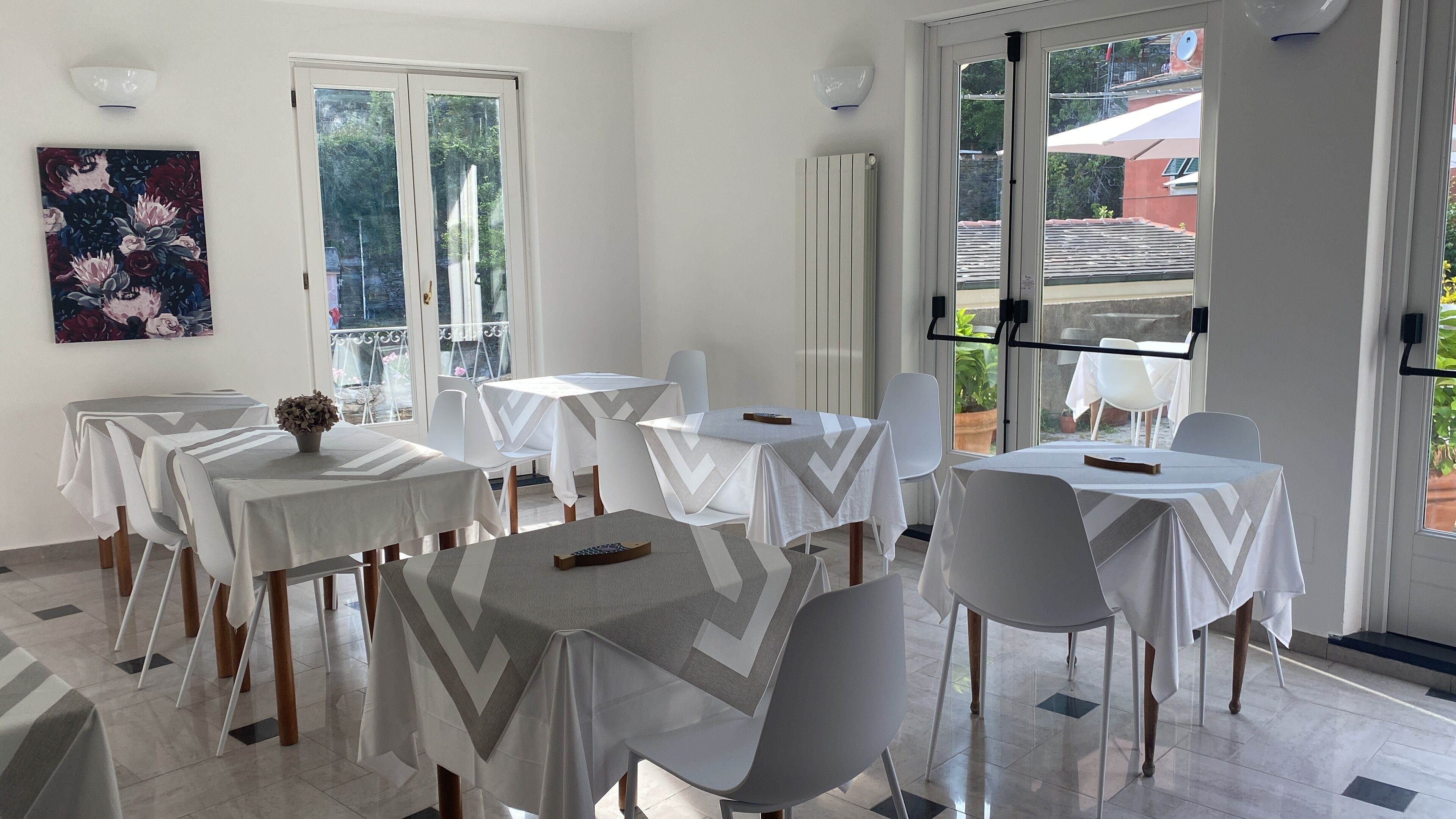 A dining area with tables and chairs, a potted plant, and a painting on the wall.