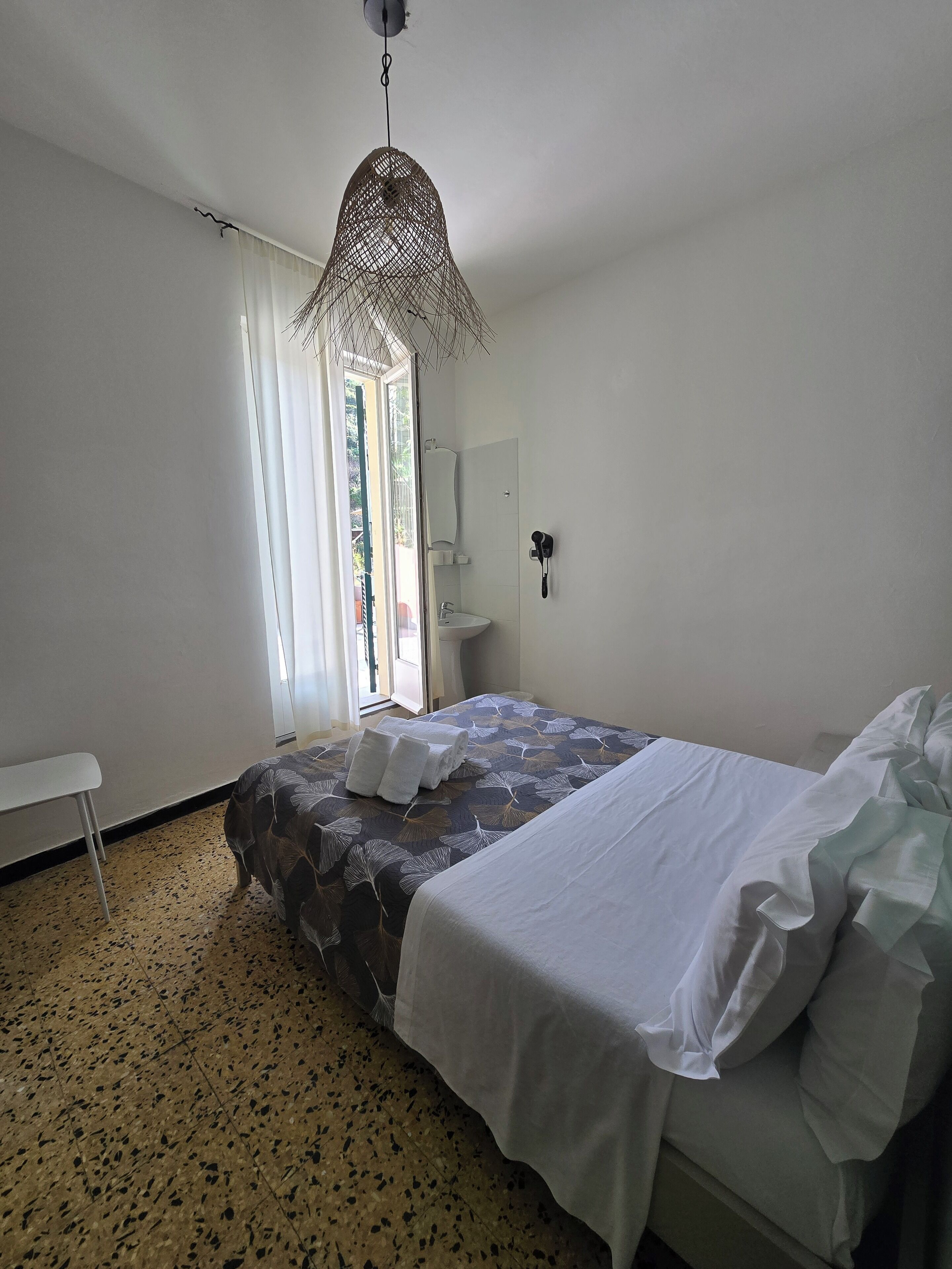 Ein Schlafzimmer mit Bett, einer Bank, einer Hängeleuchte, einem Fenster und einem Waschbecken.
