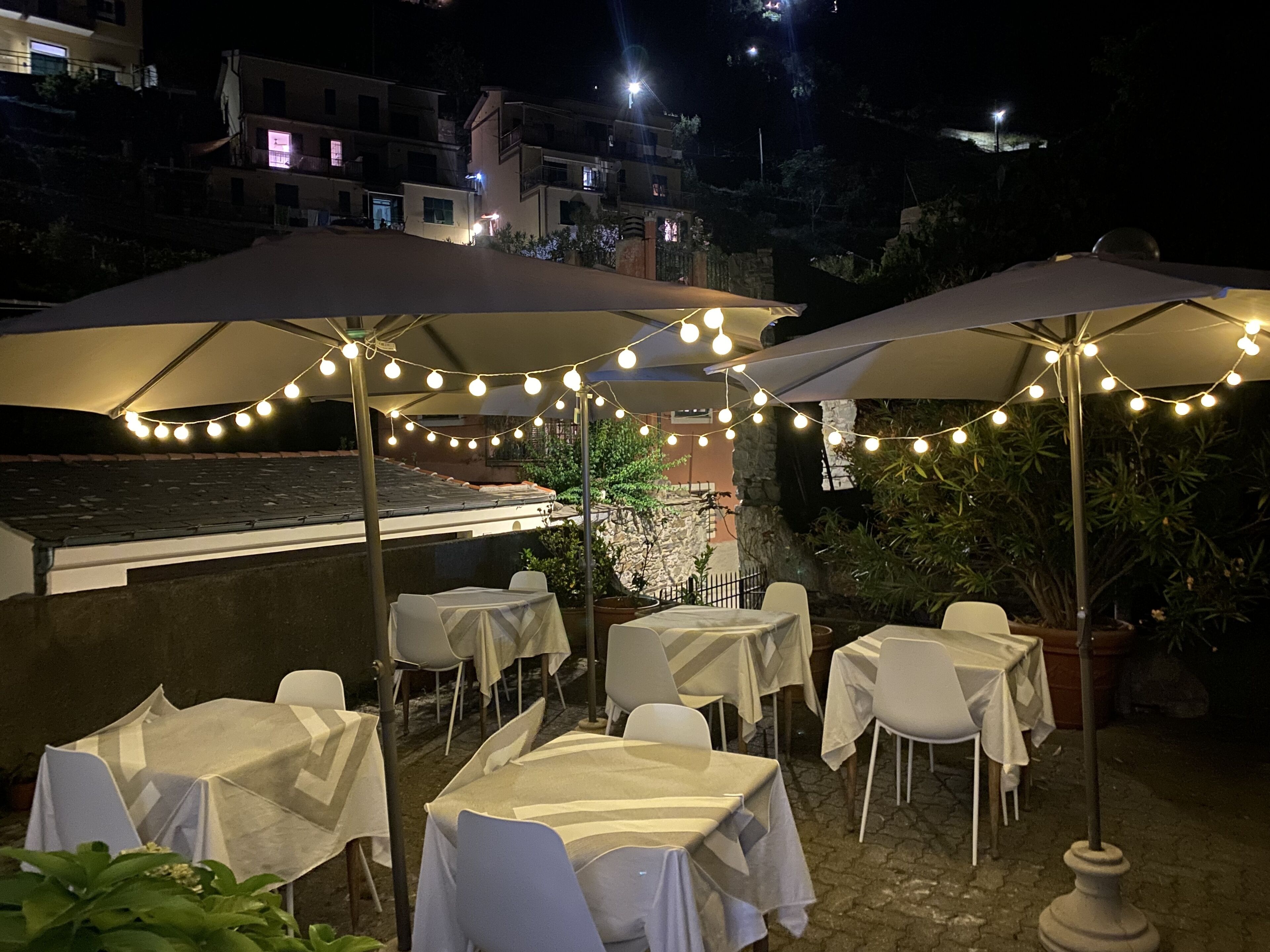 Een buiten eetgedeelte met tafels en stoelen, beschut door parasols en met lichtjes.